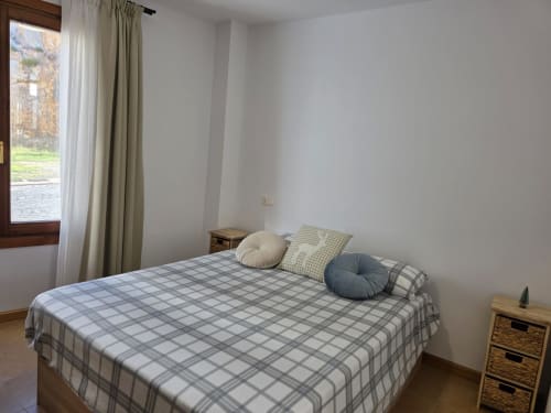 Luminosa habitación en Apartamentos el Manantial de Chóvar con ropa de cama de cuadros, ventana con vista a la montaña y almacenamiento de madera.