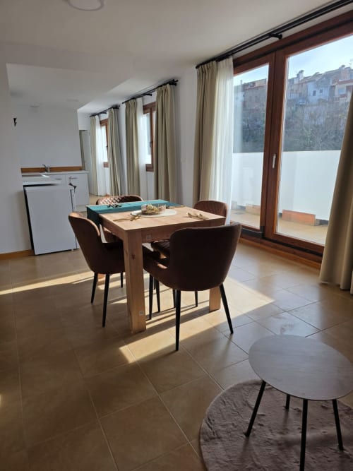Luminoso comedor con mesa de madera, sillas marrones y vistas a la montaña en Apartamentos el Manantial de Chóvar