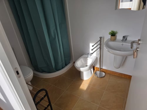 Cuarto de baño moderno en Apartamentos el Manantial de Chóvar con lavamanos pedestal blanco, bidé, inodoro y cortina de ducha verde azulada
