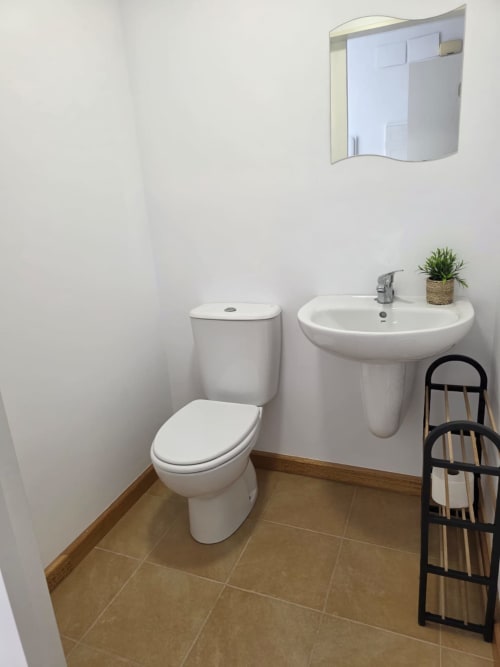 Baño moderno y limpio en Apartamentos el Manantial de Chóvar con inodoro, lavabo pedestal, espejo y piso de cerámica marrón