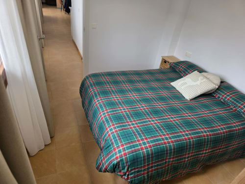 Acogedora habitación en Apartamentos el Manantial de Chóvar con ropa de cama a cuadros, almohadas blancas y piso de madera