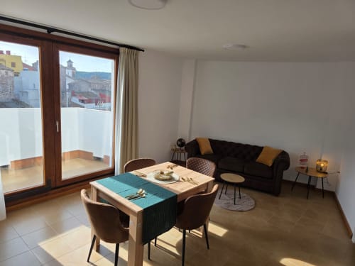 Moderna sala de estar en Apartamentos el Manantial de Chóvar con vistas a la montaña, mesa de comedor y sofá negro