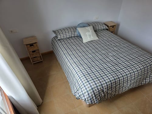 Habitación limpia en Apartamentos el Manantial de Chóvar con ropa de cama a cuadros, mesitas de noche de madera y paredes blancas