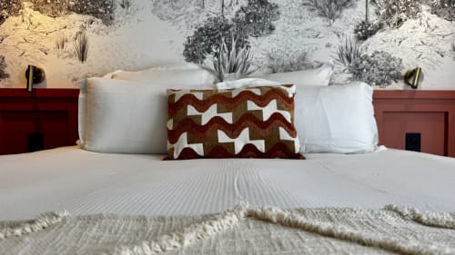 Lit king-size aux têtes de lit terracotta, oreillers blancs, coussin à motifs et œuvre désertique à l'Hôtel des Quatre