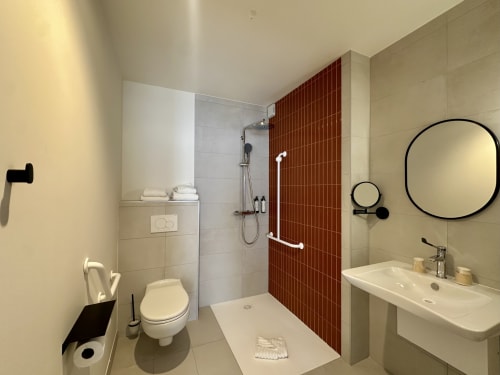 Salle de bain accessible moderne à l'Hôtel des Quatre Saisons à Guérande avec douche accessible, accents de carrelage rouge et circulaire