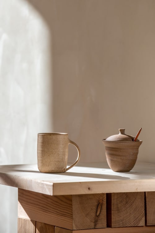 Présentation minimaliste sur table en bois à La Grange Aux Etangs avec tasse en céramique et sucrier à la lumière naturelle