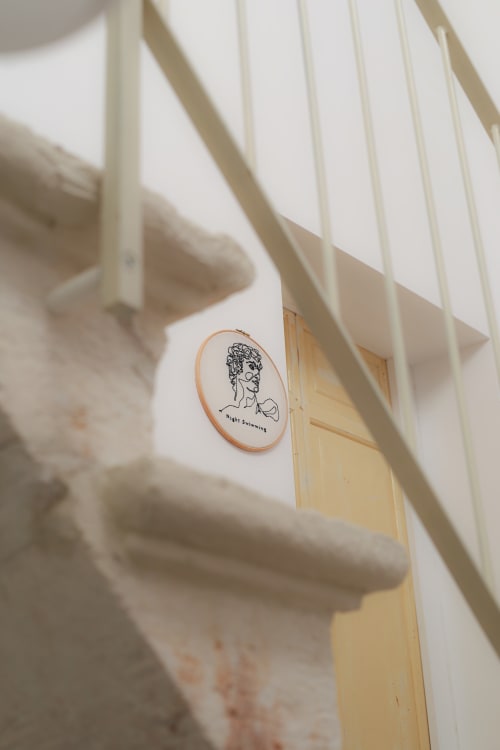 Embroidered portrait hoop art on white wall at Hotel Fragile, Ciutadella de Menorca, with sunlit blinds casting shadows