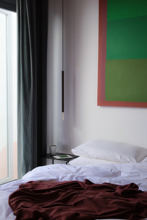 Modern hotel bedroom at Hotel Fragile in Menorca with white bedding, burgundy throw, window view, and colorful wall art