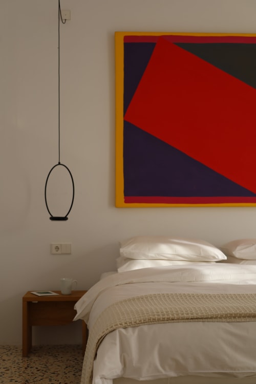 Modern bedroom at Hotel Fragile in Menorca with white bedding, wooden nightstand, geometric art, and hanging pendant light
