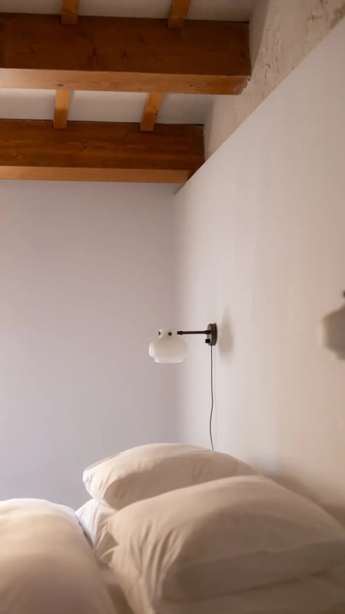 Minimalist hotel bedroom at Hotel Fragile in Menorca with white bedding, wooden ceiling beams, and wall-mounted reading