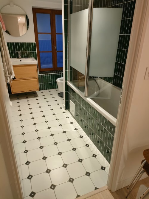 Salle de bain moderne dans un appartement messin avec douche aux carrelages verts, meuble vasque en bois et carrelage décoratif au sol
