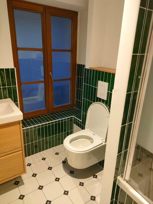 Salle de bain moderne de l'appartement Mattbnb à Metz avec carreaux verts, toilettes blanches et vue sur la ville par fenêtre bois