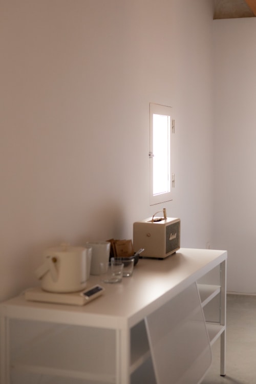 Minimalist hotel room at Hotel Fragile in Menorca with white desk, vintage radio, and natural light from door window