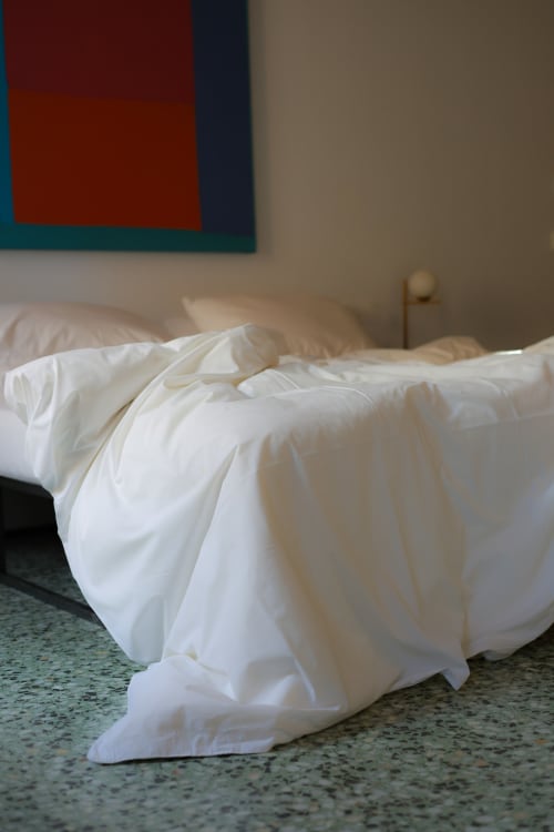 Unmade bed with white linens and colorful abstract artwork at Hotel Fragile in Menorca