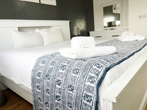 Chambre spacieuse dans un appartement à Dakar avec lit blanc, tapis motif marine et ameublements modernes