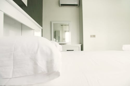 Modern bedroom in Dakar apartment with white bedding, mirror, air conditioning, and contemporary décor