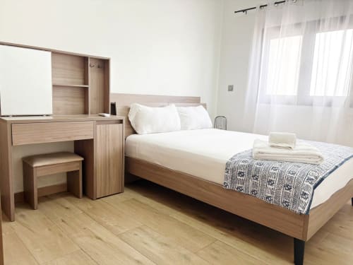 Modern bedroom at DakarByDays apartment in Dakar with wooden bed, white linens, desk, and city view windows