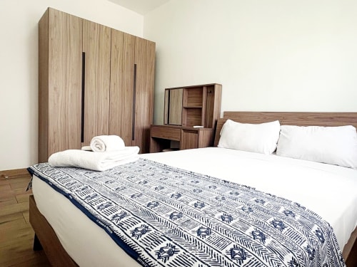 Spacious bedroom at DakarByDays apartment in Dakar with wooden wardrobe, queen bed, white linens, and patterned throw blanket