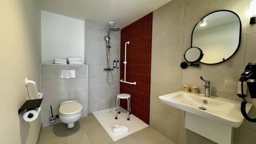 Salle de bains accessible avec douche à l'italienne, barres d'appui, toilettes, lavabo et miroir à l'Hôtel des Quatre Saisons à Guérande