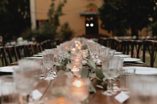 Elegante allestimento per cena all'aperto a Palazzo Bonfiglioli con tavoli lunghi illuminati a candela, bicchieri e composizioni floreali al tramonto.