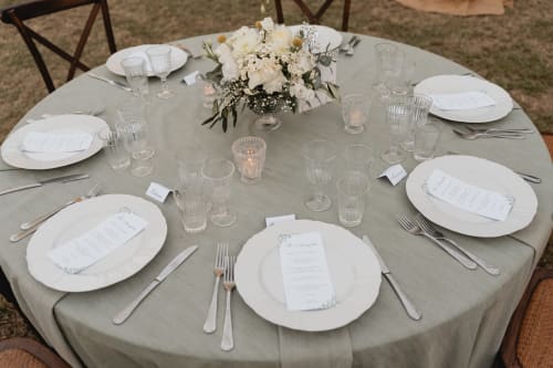Elegante tavolo da pranzo rotondo a Palazzo Bonfiglioli con piatti bianchi, mise en place, composizione floreale e menu.