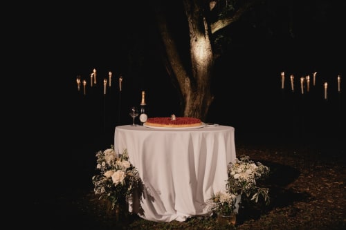 Elegante cena notturna a Palazzo Bonfiglioli con tavolo illuminato a candela, torta con rosa rossa e composizioni floreali