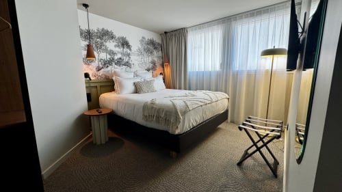 Chambre contemporaine de l'Hôtel des Quatre Saisons avec lit queen, luminaires suspendus, lampadaire et grandes fenêtres aux rideaux