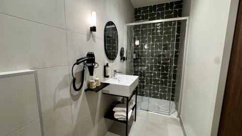 Salle de bains moderne de la suite Hôtel des Quatre Saisons Guérande avec carrelage blanc, mosaïque verte foncée à la douche, vasque et miroir