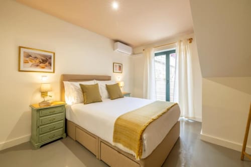 Quarto luminoso no apartamento AgapeStay Porto com cama de casal, vista para jardim pelas portas da varanda e abajur verde na cabeceira.