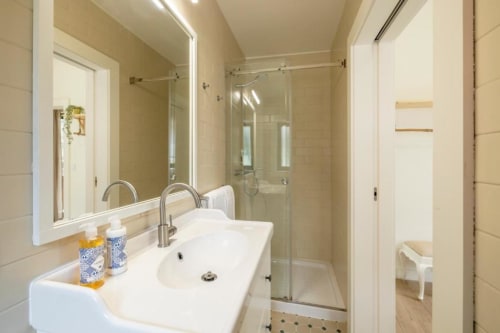 Banheiro moderno com pias duplas, espelho iluminado e duche walk-in no apartamento AgapeStay Porto com vista para jardim