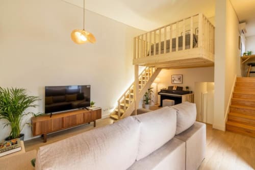 Interior moderno do apartamento no Porto com quarto em mezzanino, móveis em madeira, sofá, TV e iluminação pendente na AgapeStay