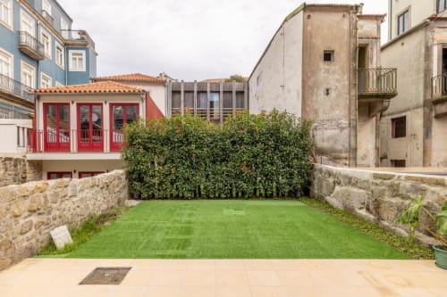 Jardim privado do AgapeStay Porto com gramado verdejante, muros de pedra e edifício com porta vermelha tradicional