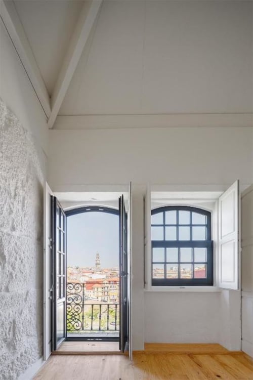 Quarto luminoso com portas francesas abertas revelando a paisagem do Porto, pisos de madeira e janela em arco com vista para a cidade na AgapeStay