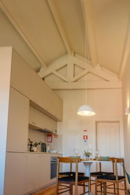 Cozinha e sala de jantar modernas em apartamento do Porto com teto abobadado, luminária branca, cadeiras de madeira e aço inoxidável
