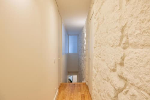 Corredor estreito com piso de madeira e parede de pedra aparente no apartamento do AgapeStay no Porto