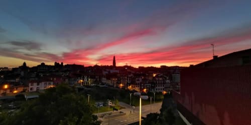 Pôr do sol vibrante sobre o cenário histórico do Porto com edifícios iluminados e campanário de igreja ao anoitecer