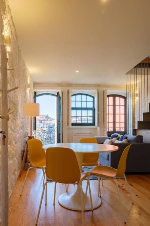 Apartamento moderno no Porto com cadeiras amarelas, mesa de jantar redonda e vistas da cidade através de janelas arqueadas com vista para o histórico