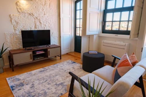 Sala de estar moderna em apartamento duplex no Porto com TV, sofá bege, puff preto, piso de madeira e vistas da cidade