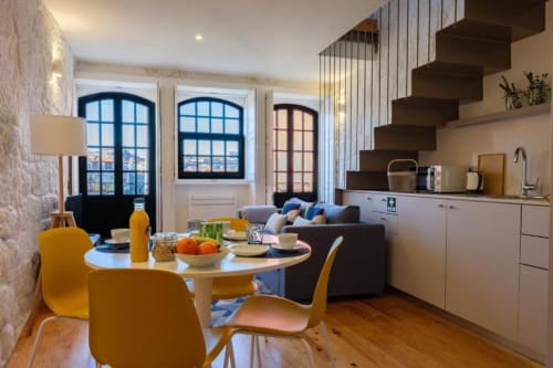 Apartamento duplex moderno no Porto com cadeiras amarelas na sala de jantar, cozinha, sofá e vista para a cidade através de janelas em arco