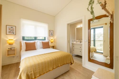 Quarto luminoso com detalhes em amarelo no apartamento térreo AgapeStay Porto, com vista para o jardim e banheiro privativo