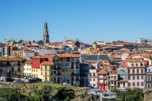 Paisagem colorida do Porto com telhados de terracota, edifícios históricos e a Torre dos Clérigos sob céu azul claro