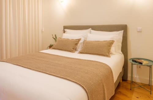 Quarto no apartamento duplex AgapeStay Porto com cabeceira estofada em bege, roupas de cama brancas, almofadas em tom tapeçaria e piso de madeira
