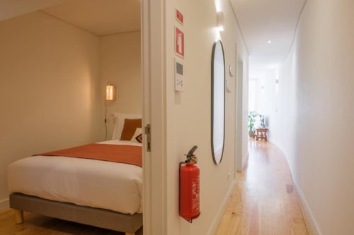 Corredor moderno em apartamento no Porto com entrada para quarto, extintor de incêndio vermelho e assoalho em madeira em direção à sala clara