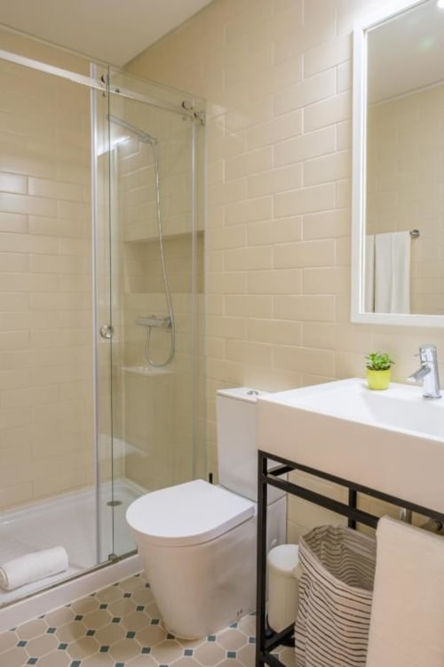 Casa de banho moderna em apartamento no Porto com azulejos subway creme, cabine de duche em vidro, sanita branca, lavatório e espelho
