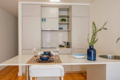 Cozinha moderna integrada com sala de jantar no AgapeStay Porto, com armários brancos, louça azul, mesa posta e plantas