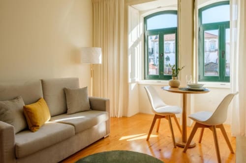 Apartamento luminoso no Porto com sofá bege, mesa de jantar em madeira, janelas verdes com vista para o jardim, assoalho em madeira e luz natural