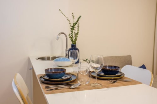 Mesa de jantar elegantemente arrumada no apartamento AgapeStay Porto com tigelas azuis, copos e flores frescas em vaso