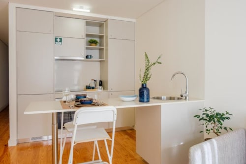 Cozinha moderna em apartamento no Porto com armários brancos, mesa de refeições, pia e plantas em vasos sobre piso de madeira
