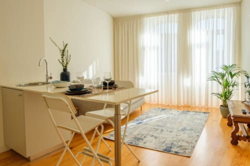 Sala de jantar moderna em apartamento no Porto com kitchenette, mesa de madeira, cadeiras creme e vista para o jardim através de janelão