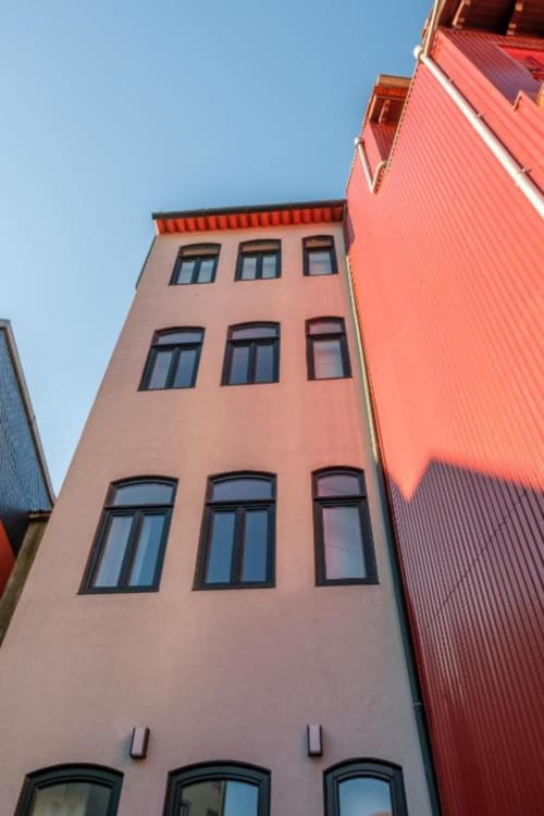 Fachada rosa-salmão do edifício de apartamentos AgapeStay Porto no Porto com janelas em fileiras e cobertura de metal ondulado vermelho